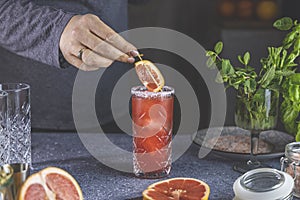 Real woman preparing pink Grapefruit Mezcal Paloma Cocktail in highball glass with water drops on table in real home. New life