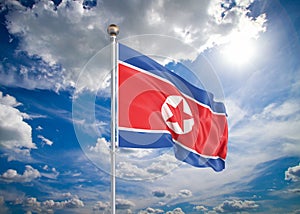 Realistic flag. 3D illustration. Colored waving flag of North Korea on sunny blue sky background