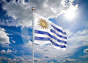 Realistic flag. 3D illustration. Colored waving flag of Uruguay on sunny blue sky background