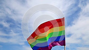 Realistic rainbow flag of an LGBT organization waving against a blue sky. LGBT pride flags include lesbians, gays