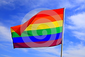 Realistic rainbow flag of LGBT organization waving against a blue sky. LGBT pride flags include lesbians, gays, bisexuals and