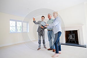 Realtor With Digital Tablet Showing Senior Couple Looking To Downsize Around Retirement Home photo