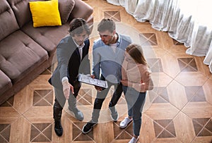 Realtor with house plan showing young couple around property for sale, above view