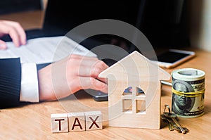 The realtor`s hand holds a bundle of money near the house with the keys. Concept of real estate tax. Payment of taxes on real est