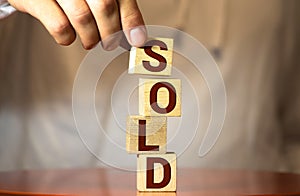 realtor& x27;s hand puts a cube with a picture of the house to the word sold. Concept of selling a house, apartment, real estate.