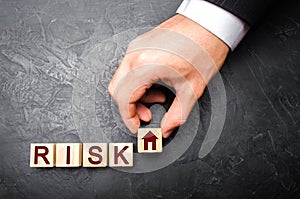 The realtor`s hand stretches a cube with a house pattern to the word risk. The concept of risk, loss of real estate.