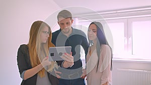 Realtor showing young caucasian couple the apartment for sale demonstrating the opportunities on tablet.