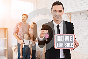 Realtor in suit holds sign with inscription. House for sale. Young family looks at apartments.