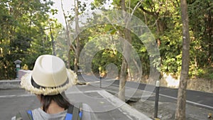 Rear back view of asian female hiker walking with backpack through tropical rain forest.