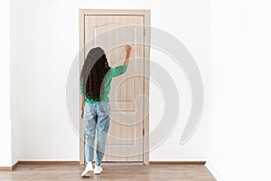 Rear back view of lady knocking on the wooden door