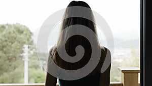 Rear back view of woman opening curtain lace standing at modern hotel looking through window