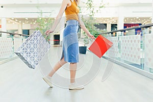 Rear Back view of a young woman with colored gift bags walking down the hallway of a mall or store. Satisfied happy blonde female