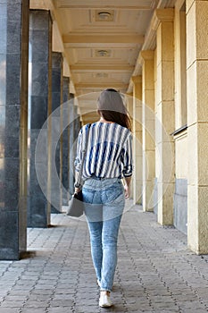 Rear Behind View Photo of Charming Lady Walking around the City. Beautiful free Woman in Skinny Jeans and Blue Blouse