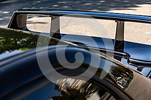 Rear black shiny car spoiler on the trunk on the pavement on a sunny day. Horizontal orientation.
