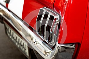 Rear chrome headlight of a red retro car. Vintage vehicle with white lines and a metal bumper. Modern tuning.