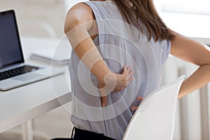 Rear closeup view girl feels backpain seated at workplace desk photo