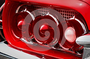 Rear cluster of an old timer luxury sports car with three tail lights with red and white glass cones, pipes framed in chrome