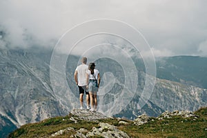 Rear of a couple enjoying a mountain covered with green grass, cloudy sky background