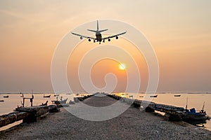 Rear image commercial passenger aircraft or cargo airplane fly over fishing wood boat floating in the sea at jetty in evening with