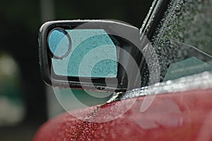 Rear mirror of a brand new red car in rainy day with droplet
