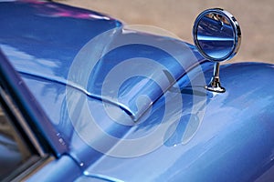 Rear mirror mounted on front fender of blue metallic color vintage car, closeup detail