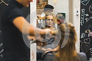 Rear mirror view of male hairdresser blowdrying long wet hair of a woman