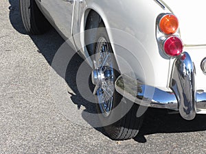 Rear of an old british classic car . Particular view of left tail light, shiny chrome bumper and left rear tire