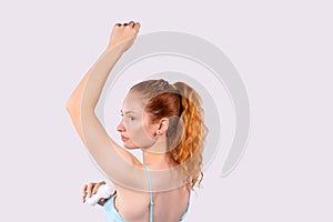 Rear photo of a red-haired young girl in home clothes who uses antiperspirant. Pure skin care for the underpads. Gray