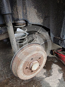 Rear rusty car disc with removed wheel, brake pad and spring close-up