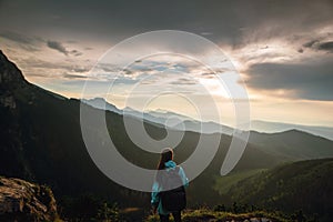 Rear shot of young packpacker woman standing on the mountain summit and enjoying beautiful sunset and Rysy mountains in Tatras, Po