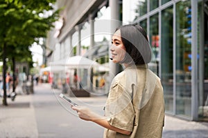 Rear shot of young woman walking in city, going down the street and smiling, holding smartphone. View from behind