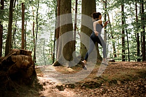 Rear side view on runner caucasian young woman wearing black sport clothes jogging in forest near tree stump photo