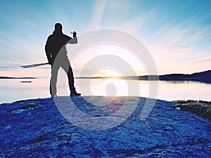 Rear silhouette of travelling man taking selfie at sea. Tourist with backpack standing on a rock