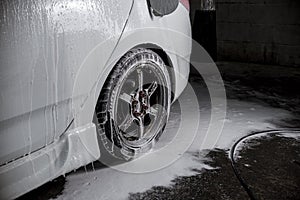 The rear tires of a white sedan dripping with soap suds prior to cleaning with water. At a car wash business