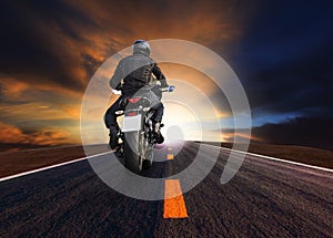 Rear veiw of young man riding big motorcycle on asphalt road against beautiful dusky sky photo