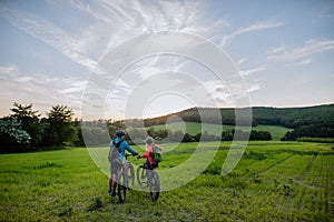 Rear view of active senior couple riding electric bicycles on trail at summer park, healthy lifestyle concept.