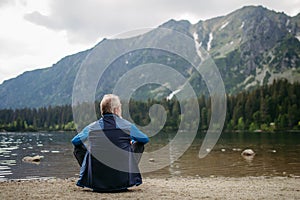 Rear view of active senior man resting after hiking in autumn mountains.