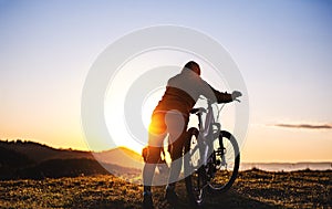 Rear view of active senior woman with bicycle outdoors in nature at sunset.