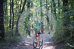 Rear view of active senior woman biker cycling outdoors in forest.