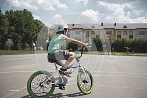 Rear view active sporty boy in sports helmet confidently riding bike. A school age child cycling on city asphalt road