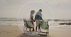 Rear view of African American couple relaxing together on a sun lounger at beach 4k