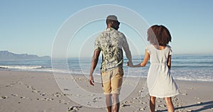 Rear view of African American couple walking side by side at beach