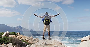 Rear view of african american man standing on rock with arms wide open while trekking in the mountai