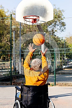 Rear view of African American man in a wheelchair throwing basketball in court.