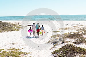 Rear view of african american parents and children walking on sandy beach against clear sky