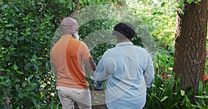 Rear view of african american senior couple holding hands walking together in the garden