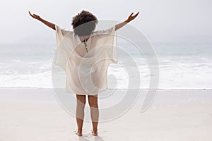 Woman standing with arms outstretched on beach in the sunshine photo