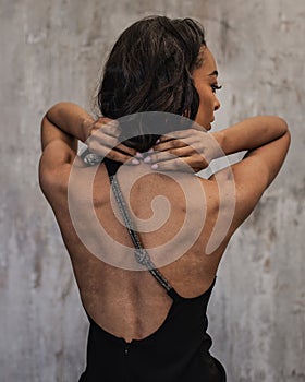 Rear view of an african american woman standing at grey wall and wearing black dress