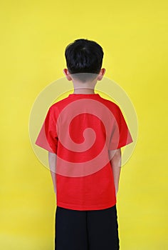 Rear view of Asian boy age 6 year old isolated on yellow background