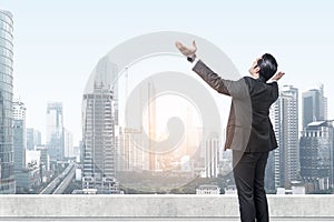 Rear view of Asian businessman standing with raised hand on the rooftop